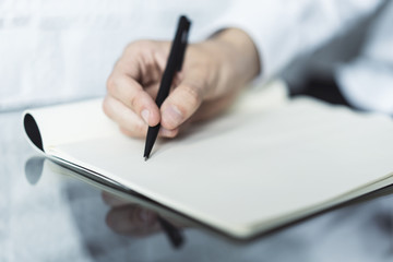 Closeup of man hand writing in diary on a glass table. Focused on a hand with pen