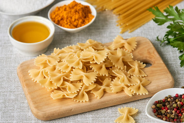 Raw farfalle pasta and spices on a gray background