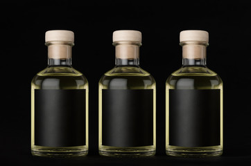 Three glass bottles for cosmetic, perfume, drink with black label, cork, yellow liquid in a row on dark black background, mock up for design of product.