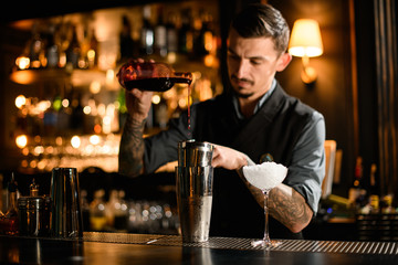 Male bartender pouring an alcoholic drink from the glass bottle to a steel shaker