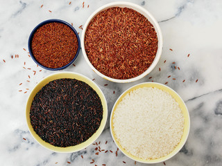 Ceramic bowls filled with a variety of grain and rice including red quinoa, red rice, black rice, and white rice on a marble top.  