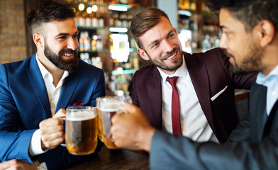 Handsome businessmen are drinking beer, talking and smiling while resting at the pub