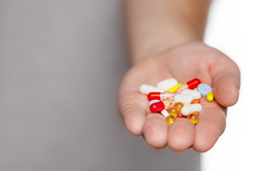 Man in gray t-shirt hold pile of various colorful multicolored pills in hand. Medicines, vitamins, antibiotics and medicaments. Selective focus. Copy space. First aid treatment and healthcare concept.