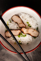 Composition with a bowl of rice noodles, meat and vegetables