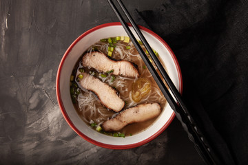 Composition with a bowl of rice noodles, meat and vegetables