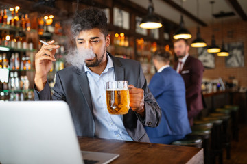 Man drinking beer and smoking cigarette while working on computer. Bad habit concept.