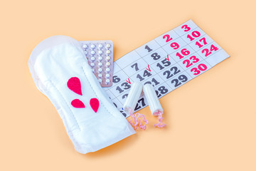 Protective menstrual pads, cotton tampons, contraceptive pills  and calendar of menstruation period on orange background. The concept of women gynecological health and intimate hygiene. Close up