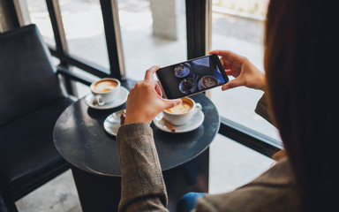 A woman using mobile phone to take a photo of coffee and snack before eat in cafe