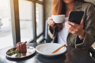 Closeup image of a woman holding and using mobile phone while drinking coffee in cafe