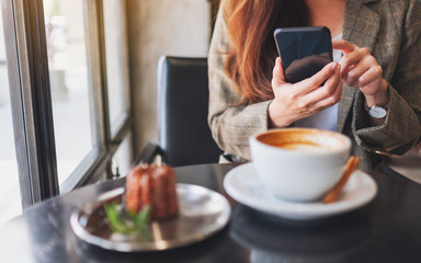 Closeup image of a woman holding and using mobile phone with coffee cup and snack on the table in cafe