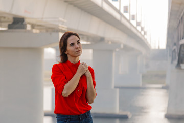 Beautiful girl stands at the bridge near the river.