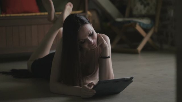 Young woman lying on the floor and reading news on tablet