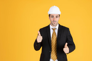Young handsome businessman wears suit and construction helmet on isolated yellow background.
