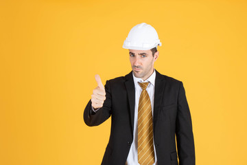 Young handsome businessman wears suit and construction helmet on isolated yellow background.