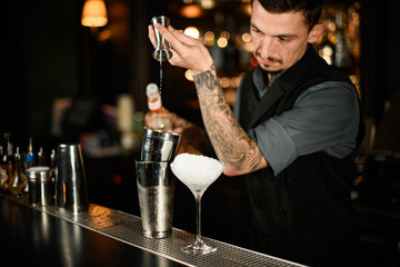 Bartender pouring an alcoholic cocktail drink from the jigger to a steel shaker