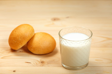 A glass of milk and two buns on a wooden background