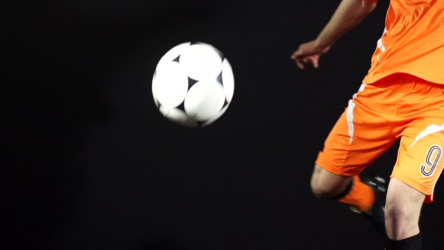 Man kicking a soccer ball / football on a Black Background. He volleys the unbranded ball past the camera. Super Slow motion