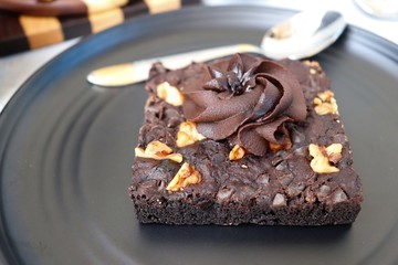 Homemade chocolate walnut brownie on dark plate garnished with chocolate ganache and walnuts. Copy space.