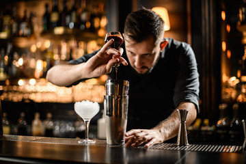 Bartender pouring a dark brown bitter from the glass bottle to a steel shaker