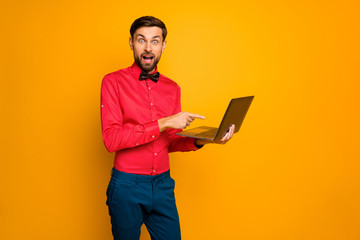 Photo of crazy excited business guy hold notebook read email new project boss approval direct finger screen wear trendy red shirt bow tie blue pants isolated yellow color background