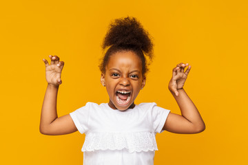 Funny afro little girl imitating tiger over yellow background
