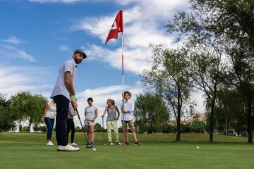 Man playing golf in front of a red-flagged hole and a group of people watching