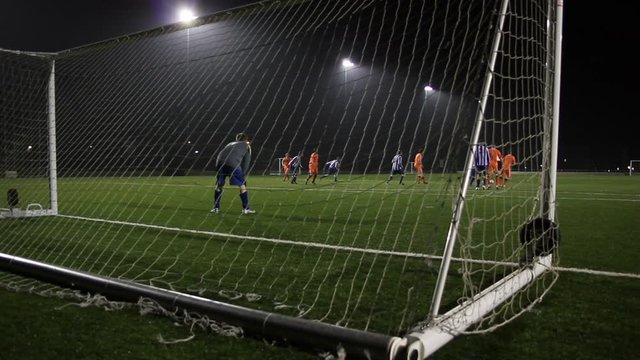 Scoring a Goal during a Football / Soccer Match. The player kicks the ball past the goalkeeper. Behind the net