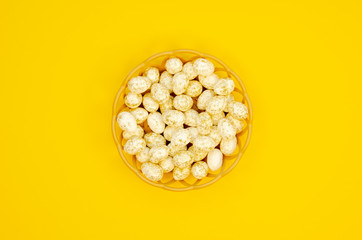 A basket in the shape of a nest with quail Easter eggs. Top view of white eggs in a golden speck on yellow background