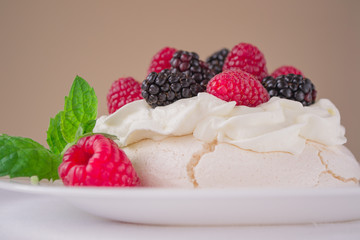 Mini Pavlova meringue cake with berries and mint on white plate.