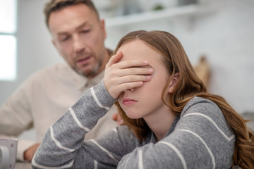 Fototapeta premium Long-haired girl in grey shirt closing her eyes with her hand