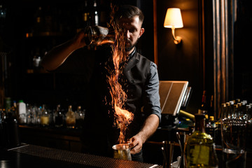 Bartender pouring a transparent alcoholic drink from the one steel cup to another making a fire
