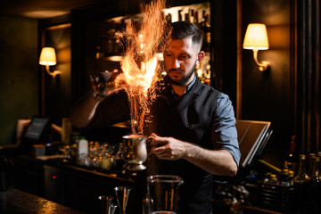 Bartender pouring a burning alcoholic drink from the one steel cup to another