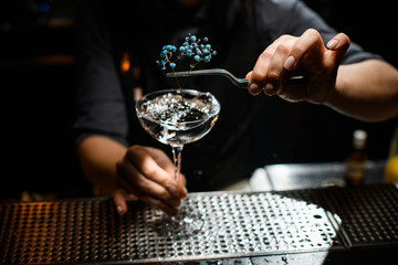Bartender girl decorating an alcoholic cocktail in the glass with a dried flower by tweezers