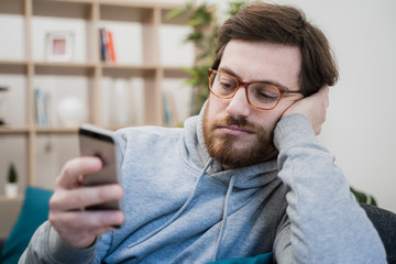 Single lonesome man checking mobile phone on the couch