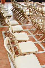 Many empty white wooden chairs lined up for a retro style event.