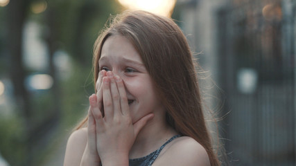 Close-up shooting of attractive young green-eyes girl. Teenage girl in green clothes laughing to tears. Outdoors. Summertime. Green blurred background.