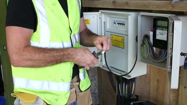 Electrician working at Fuse box and is doing some wiring. The technician is wearing a hard hat and hi vis jacket. Close up.  - Stock Video clip footage. 