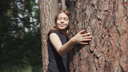 Adorable nature child hugging a tree in the beautiful sunny forest. Portrait of a lovable girl embracing tree trunk caring for the environment.