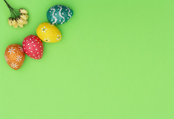 Colorful painted orange, blue, red and yellow Easter eggs with yellow spring flowers on green background. Happy Easter holiday concept. Flat lay style with copy space.