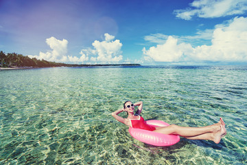 Enjoying suntan and vacation. Outdoor portrait of pretty young woman in red swimsuit on inflatable ring on tropical beach.