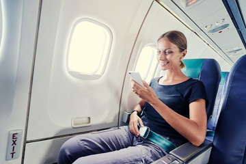 Travel and technology. Young woman in plane using smartphone while sitting in airplane seat.