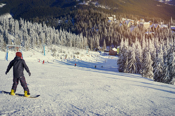 Snowy mountains and ski lifts. Skiers and snowboarders skiing downhill to village.