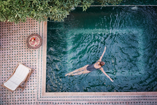 Enjoying bathing. Vacation concept. Top view of young woman in the private swimming pool in beautiful moroccan backyard.