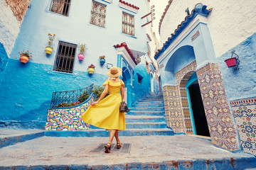 Colorful traveling by Morocco. Young woman in yellow dress walking in  medina of  blue city...
