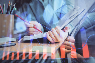 A woman hands writing information about stock market in notepad. Forex chart holograms in front. Concept of research. Multi exposure