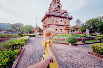 Follow me. Travel by Asia. Young woman in hat and yellow dress walking near the Chalong buddhist temple on Phuket Island in Thailand.