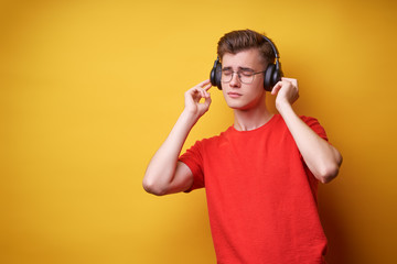 Enjoying the sound. Colorful portrait of happy young man with earphones is listening music against yellow background.