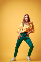 Colorful studio portrait of happy young girl dancing against yellow background.