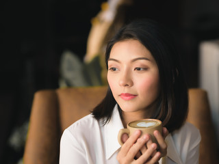 A black haired asian woman is resting and refreshing coffee in the morning.