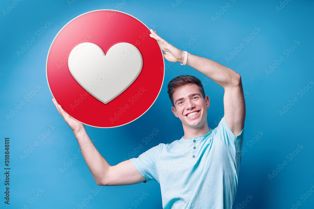 Wall mural Colorful studio portrait of young man holding love empathetic emoji reaction, printed on paper.